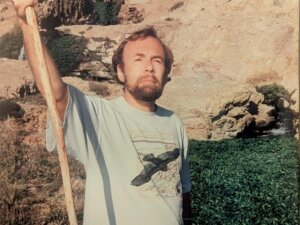 Man holds walking stick near rock formation